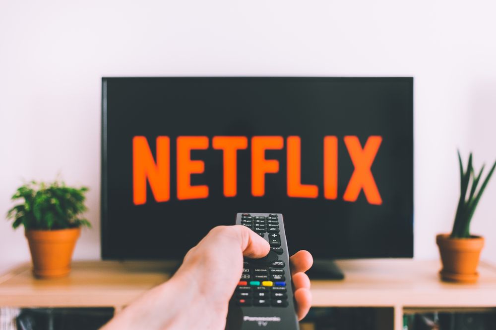 Hand holding a streaming remote control in front of a television